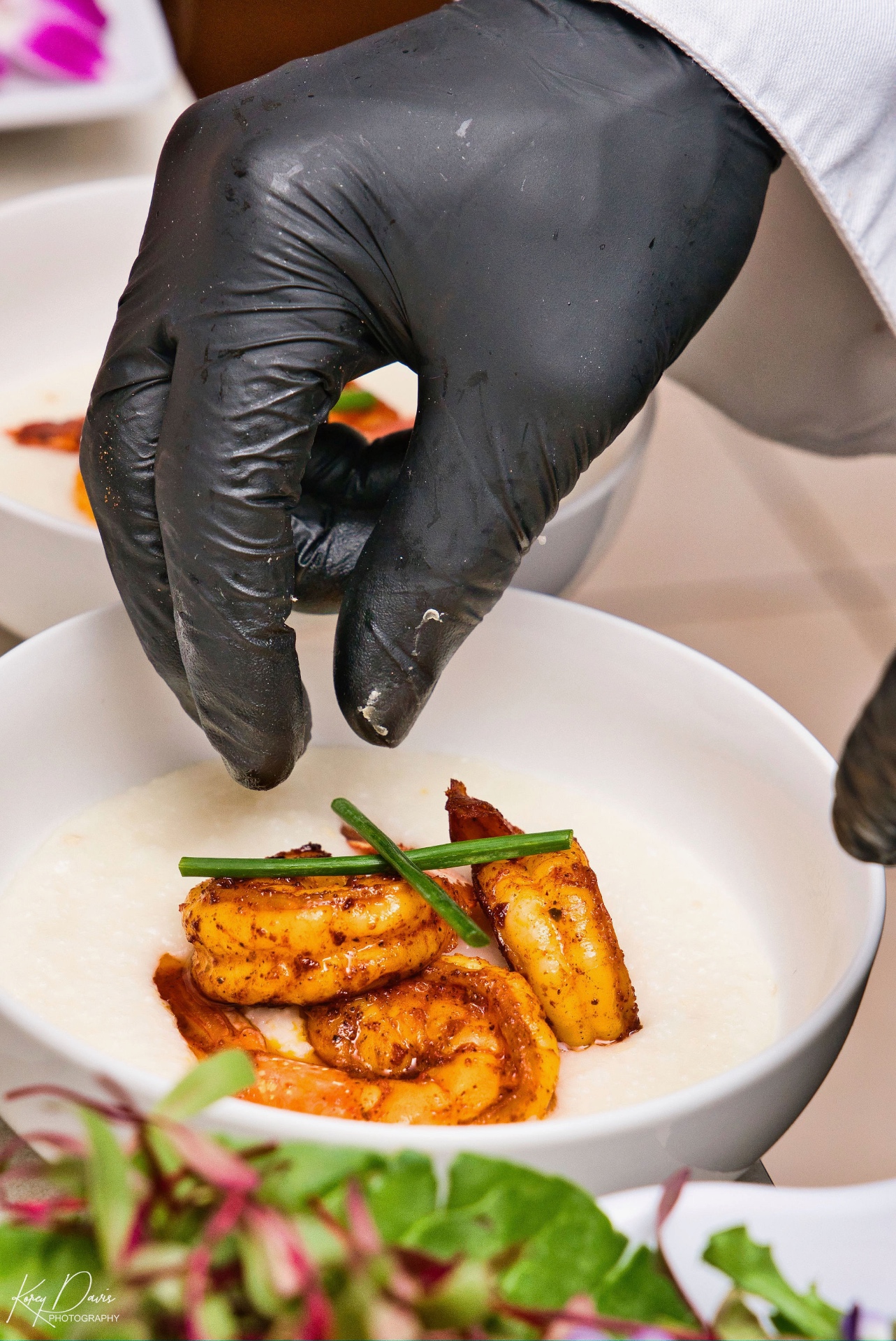 Chef finishing a bowl of shrimp and grits by hand during service