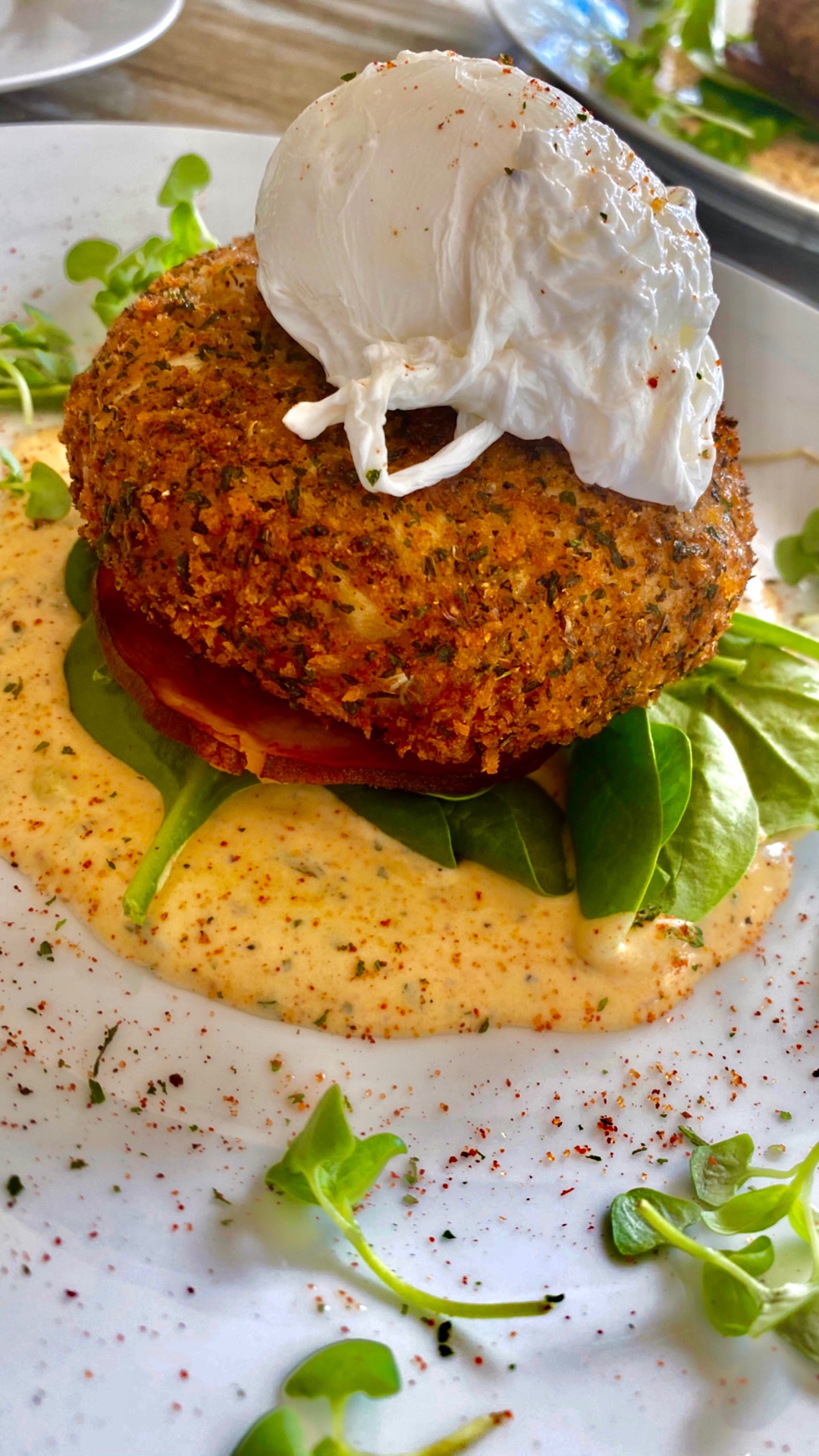 Crab cake Benedict with a poached egg, greens, tomato, and cream sauce